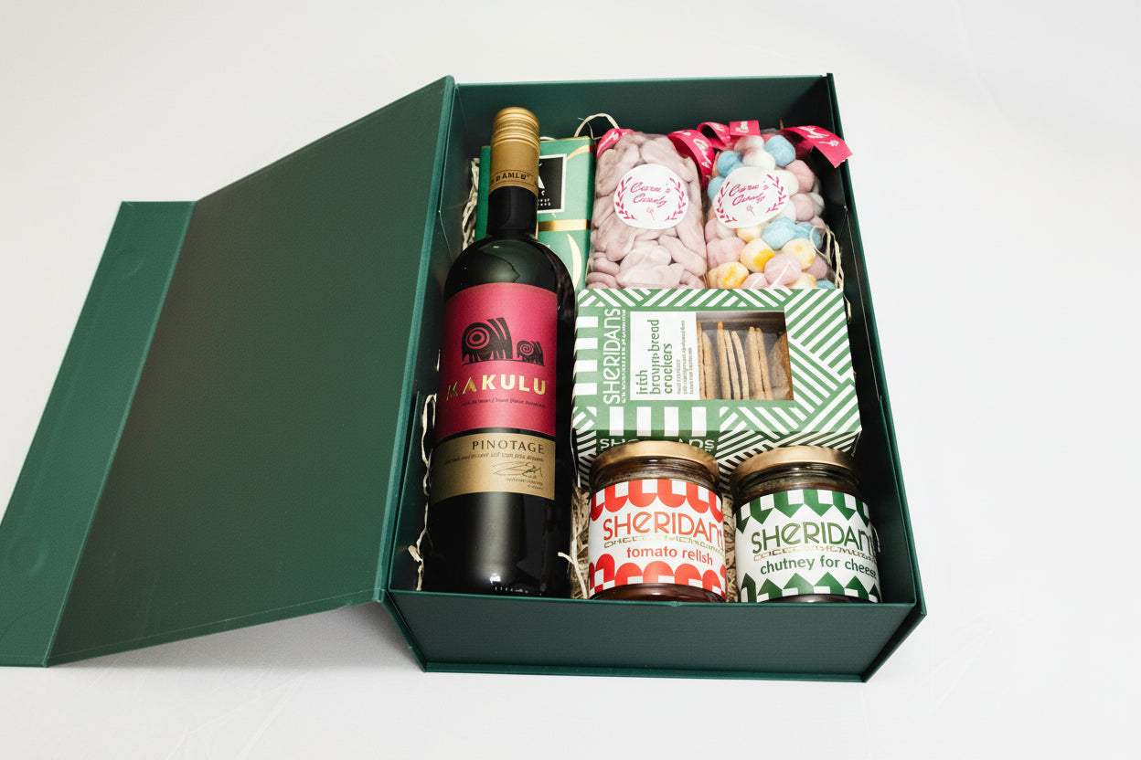 A green magnetic box containing a variety of Christmas treats including wine, chocolates, crackers, and condiments.